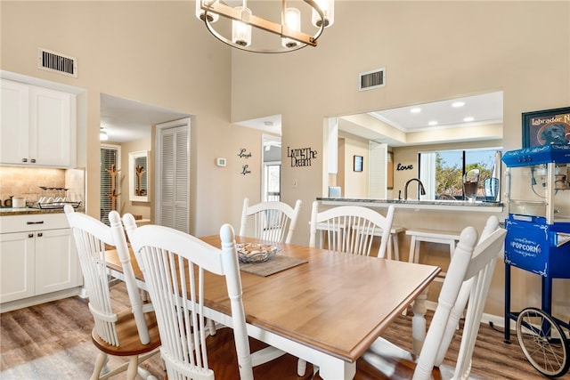 dining area with a chandelier, sink, light hardwood / wood-style floors, and a raised ceiling