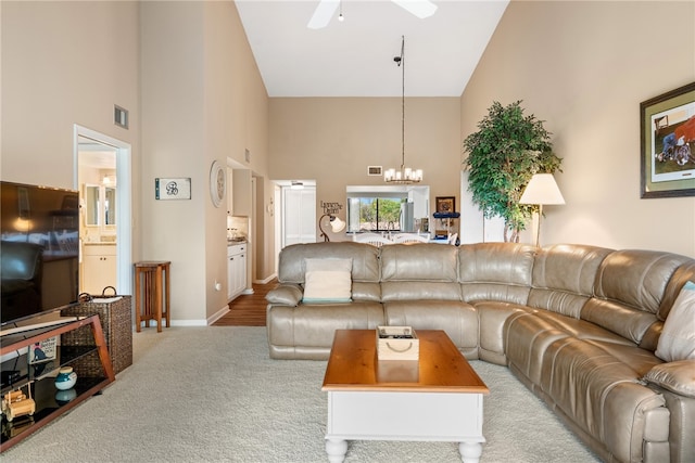 living room featuring high vaulted ceiling, ceiling fan with notable chandelier, and light carpet