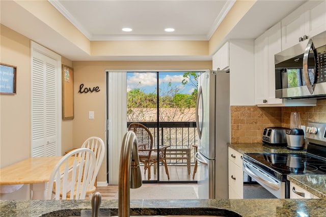 kitchen with dark stone countertops, appliances with stainless steel finishes, ornamental molding, and white cabinets