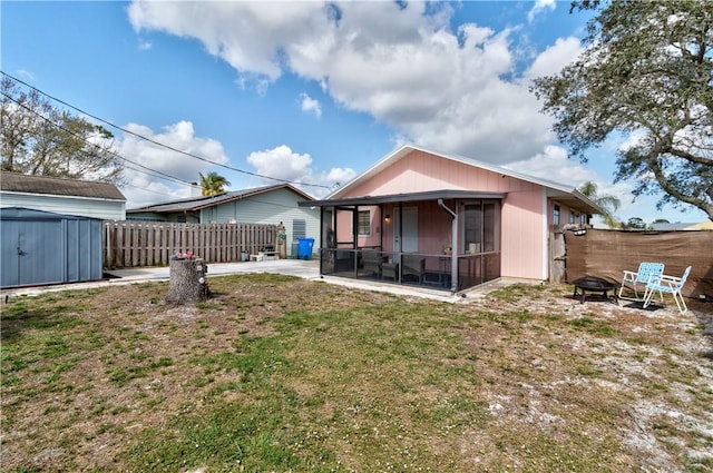 back of house with a storage shed, a patio area, a yard, a fire pit, and a sunroom