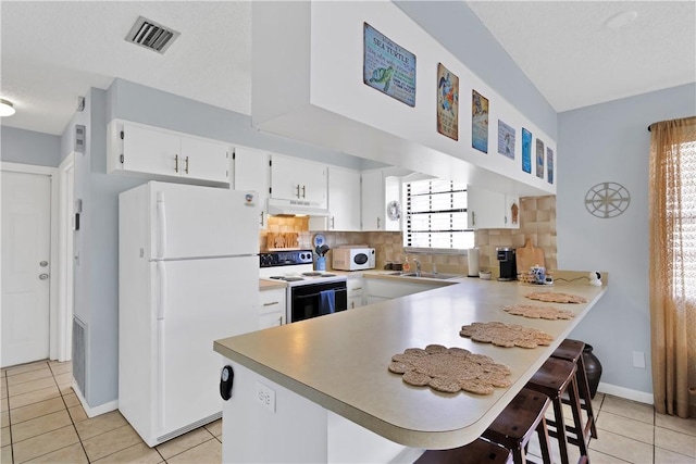 kitchen with white appliances, a kitchen breakfast bar, kitchen peninsula, and white cabinets