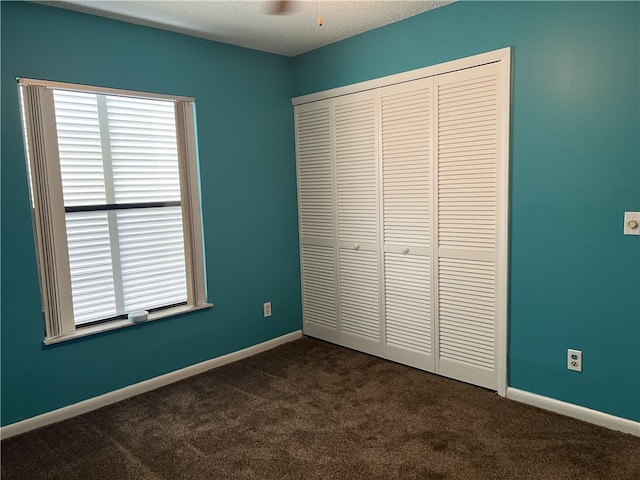 unfurnished bedroom featuring ceiling fan, dark colored carpet, a closet, and a textured ceiling