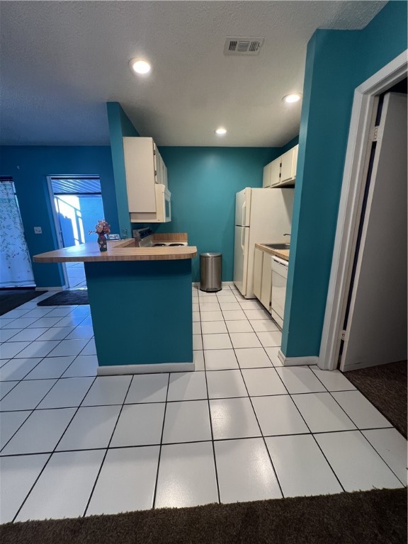 kitchen with white cabinetry, kitchen peninsula, a kitchen breakfast bar, a textured ceiling, and light tile patterned floors