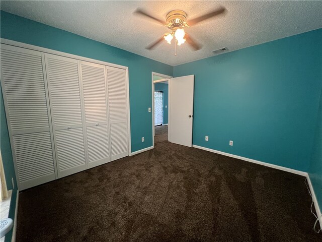 unfurnished bedroom featuring a textured ceiling, dark colored carpet, ceiling fan, and a closet