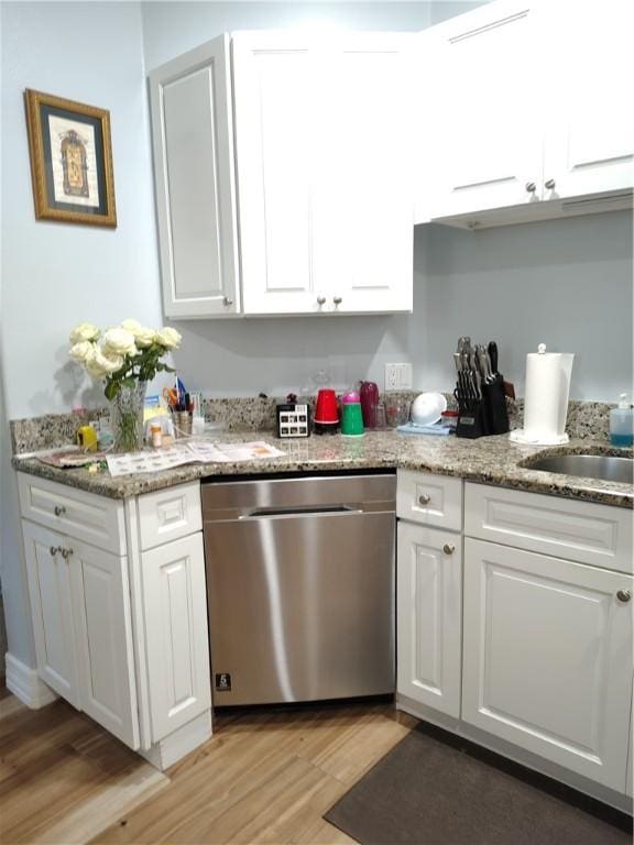 kitchen with light stone counters, white cabinetry, stainless steel dishwasher, and light hardwood / wood-style flooring