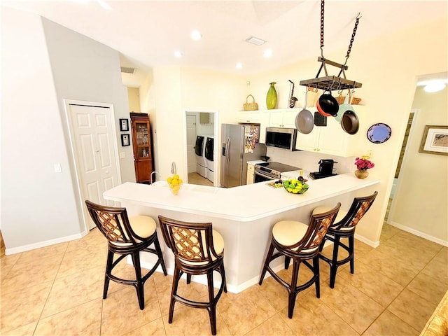 kitchen featuring white cabinetry, a breakfast bar area, kitchen peninsula, stainless steel appliances, and washing machine and dryer