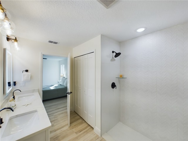 bathroom with a textured ceiling, vanity, tiled shower, and wood-type flooring