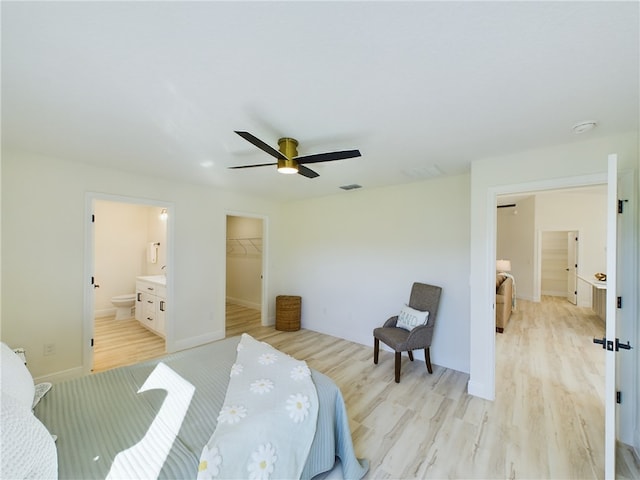 bedroom with light hardwood / wood-style flooring, a walk in closet, a closet, ensuite bathroom, and ceiling fan