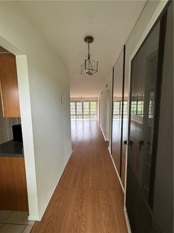 corridor with a notable chandelier, wood finished floors, and baseboards