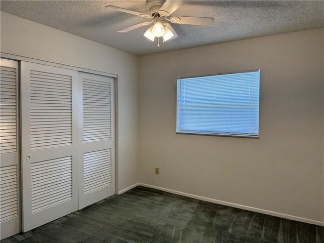 unfurnished bedroom with ceiling fan, a closet, a textured ceiling, and dark colored carpet