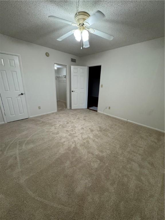 unfurnished bedroom featuring baseboards, ceiling fan, a textured ceiling, a walk in closet, and light colored carpet