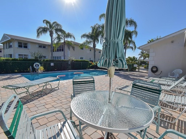 community pool with a patio area, fence, and outdoor dining space