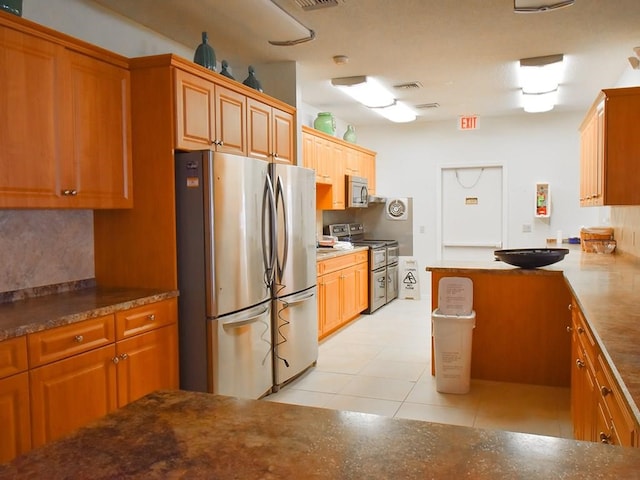 kitchen with appliances with stainless steel finishes, brown cabinetry, backsplash, and light tile patterned floors