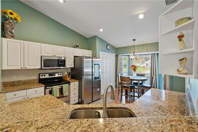 kitchen featuring lofted ceiling, a sink, appliances with stainless steel finishes, white cabinetry, and a chandelier