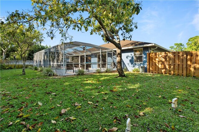 rear view of house featuring glass enclosure, a lawn, and fence