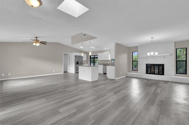 unfurnished living room with a brick fireplace, ceiling fan with notable chandelier, a textured ceiling, vaulted ceiling, and hardwood / wood-style floors