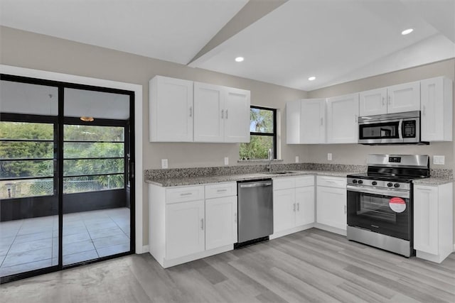 kitchen featuring white cabinets, appliances with stainless steel finishes, light stone counters, and lofted ceiling