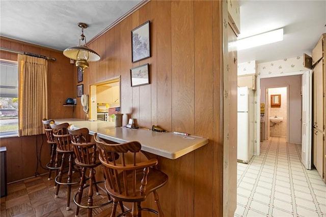 bar featuring white fridge, wood walls, and hanging light fixtures