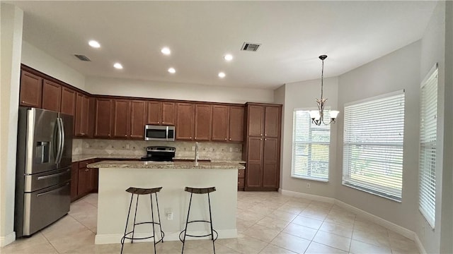 kitchen featuring a breakfast bar, light stone counters, a center island with sink, stainless steel appliances, and backsplash