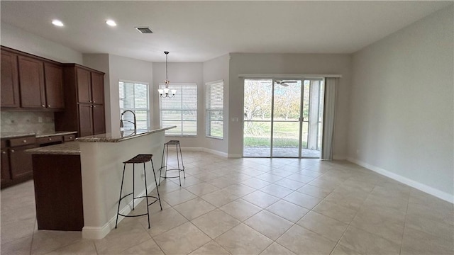 kitchen with stone counters, a breakfast bar, a center island with sink, and a chandelier