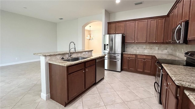 kitchen with sink, stainless steel appliances, light stone countertops, a kitchen island with sink, and decorative backsplash