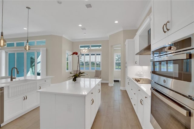 kitchen with appliances with stainless steel finishes, a center island, ornamental molding, white cabinetry, and decorative light fixtures