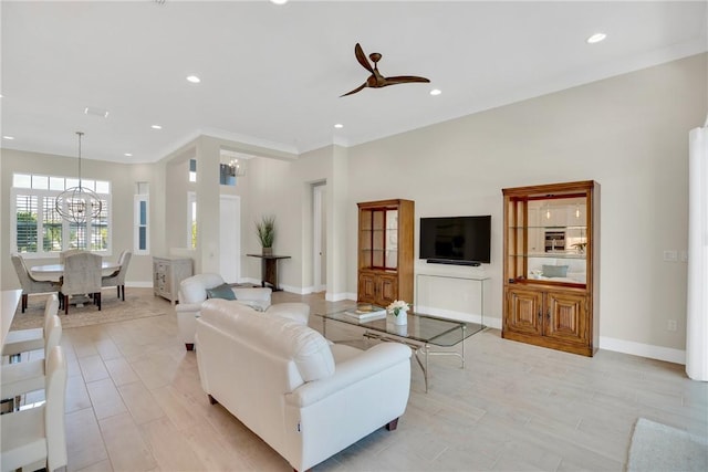 living room with ceiling fan with notable chandelier, ornamental molding, and light hardwood / wood-style floors