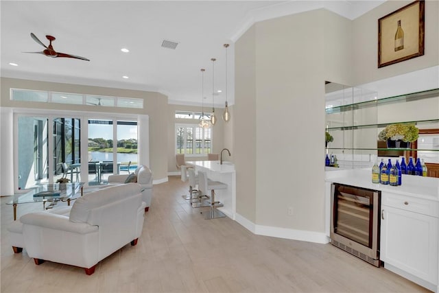 living room featuring light hardwood / wood-style floors, bar, wine cooler, ornamental molding, and ceiling fan