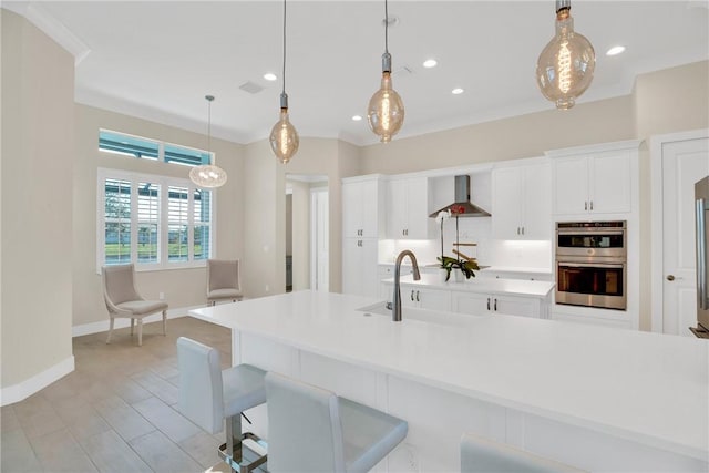 kitchen featuring pendant lighting, stainless steel double oven, wall chimney exhaust hood, sink, and white cabinetry