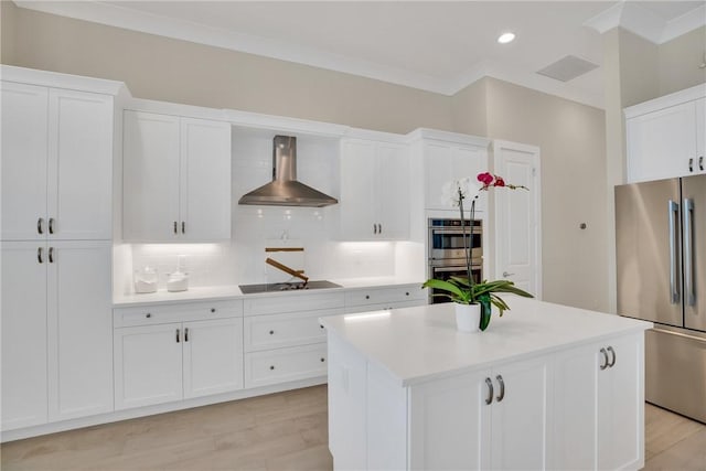 kitchen featuring appliances with stainless steel finishes, a center island, wall chimney exhaust hood, white cabinetry, and tasteful backsplash