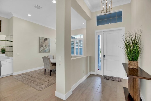 foyer entrance with ornamental molding, light hardwood / wood-style floors, and a notable chandelier