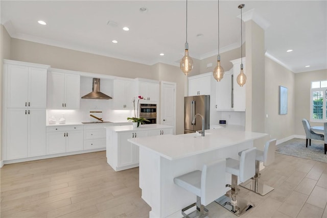 kitchen featuring wall chimney exhaust hood, hanging light fixtures, stainless steel appliances, a kitchen bar, and white cabinetry