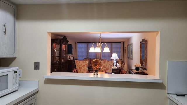 kitchen with hanging light fixtures, white microwave, a chandelier, and light countertops