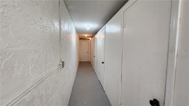 hallway with a textured ceiling, a textured wall, and concrete flooring