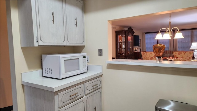 kitchen featuring hanging light fixtures, white microwave, light countertops, and a notable chandelier