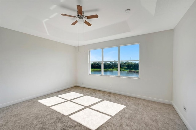 empty room featuring a tray ceiling, ceiling fan, a water view, and light colored carpet