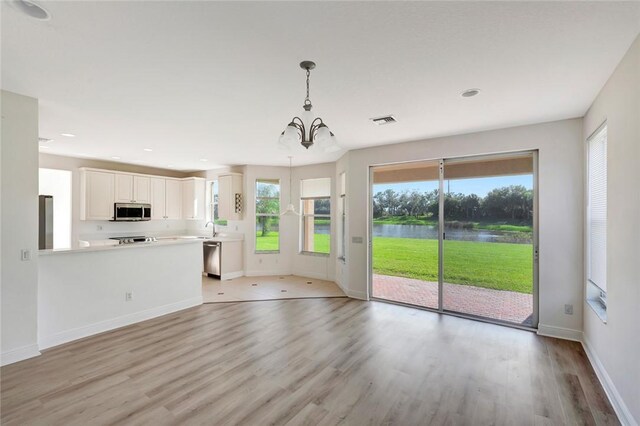 unfurnished living room with plenty of natural light, a water view, light hardwood / wood-style flooring, and an inviting chandelier