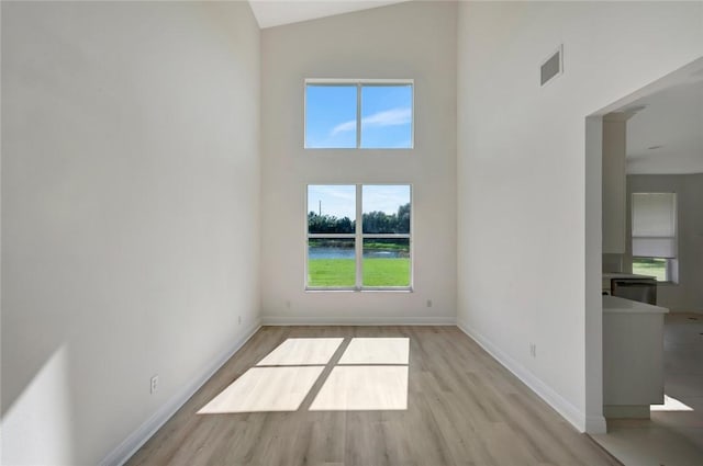 unfurnished room with high vaulted ceiling and light hardwood / wood-style flooring