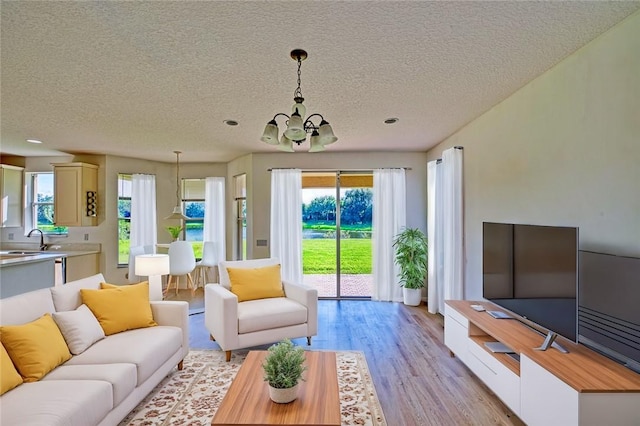 living room featuring a textured ceiling, light hardwood / wood-style flooring, a notable chandelier, and sink