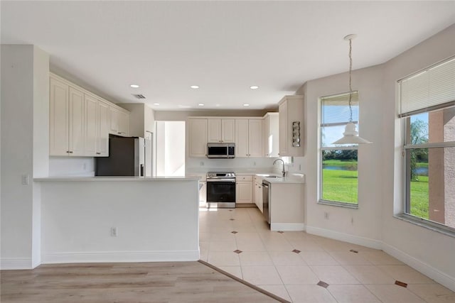 kitchen featuring hanging light fixtures, light tile patterned floors, white cabinetry, kitchen peninsula, and stainless steel appliances