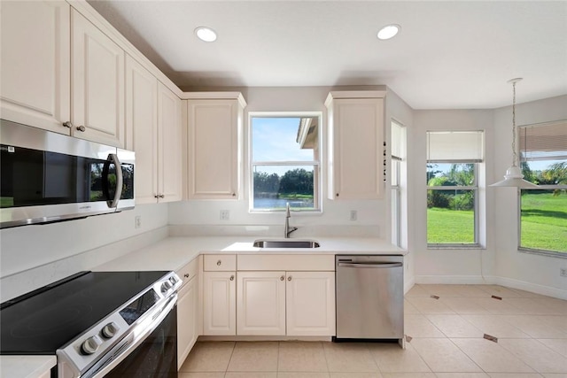 kitchen featuring white cabinets, sink, hanging light fixtures, light tile patterned floors, and stainless steel appliances