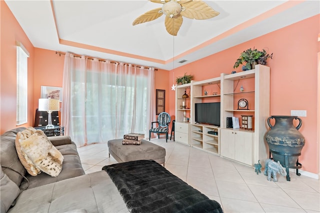 tiled living room with ceiling fan and a raised ceiling