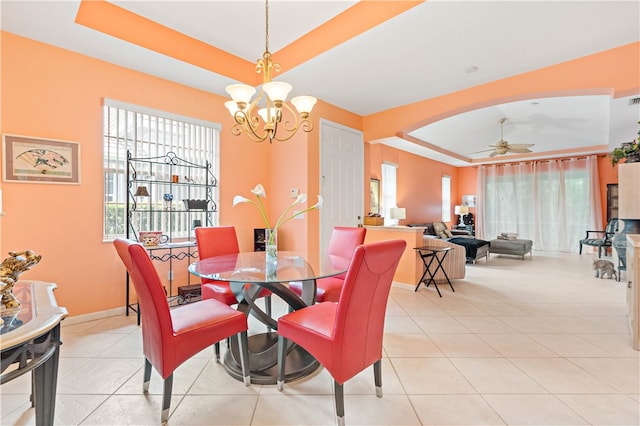 tiled dining space featuring a tray ceiling and ceiling fan with notable chandelier