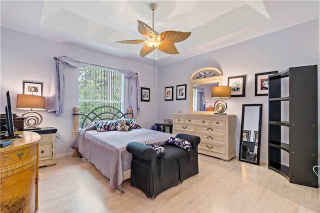 bedroom with a tray ceiling, ceiling fan, and light hardwood / wood-style flooring