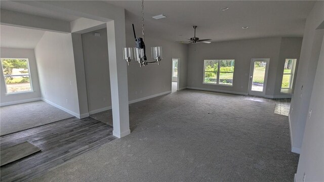 unfurnished living room with carpet flooring, baseboards, a chandelier, and healthy amount of natural light