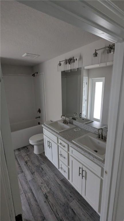full bath featuring wood finished floors, toilet, double vanity, and washtub / shower combination