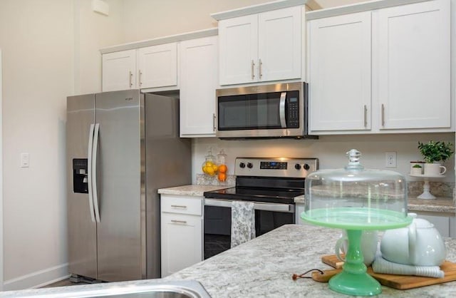 kitchen with white cabinetry, stainless steel appliances, baseboards, and light stone countertops