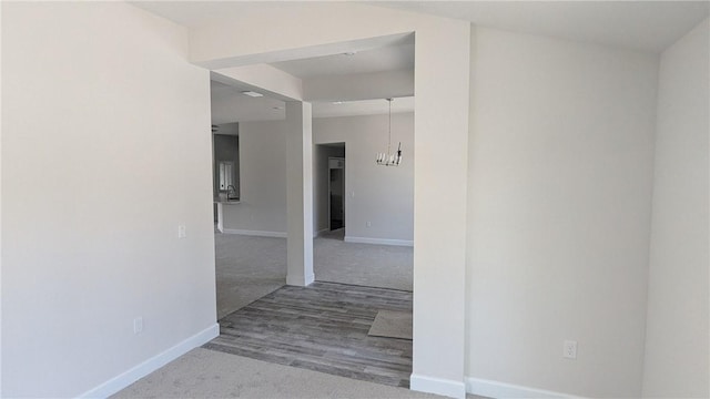 corridor featuring carpet, baseboards, and a chandelier