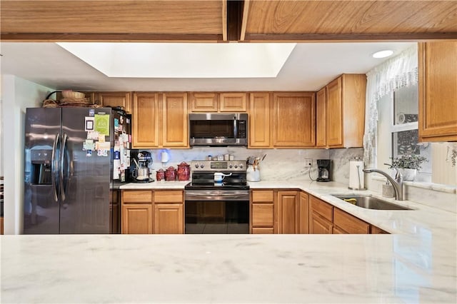 kitchen featuring backsplash, light stone countertops, a tray ceiling, stainless steel appliances, and a sink