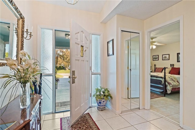 foyer entrance featuring light tile patterned floors, baseboards, a textured ceiling, and a ceiling fan